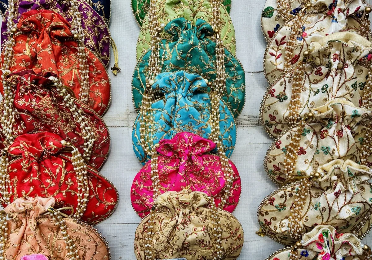 حقائب يد نسائية صغيرة مطرّزة بالأحمر والفيروزي والوردي والذهبي، بمقابض من الخرز، معروضة في صفوف على جدار متجر